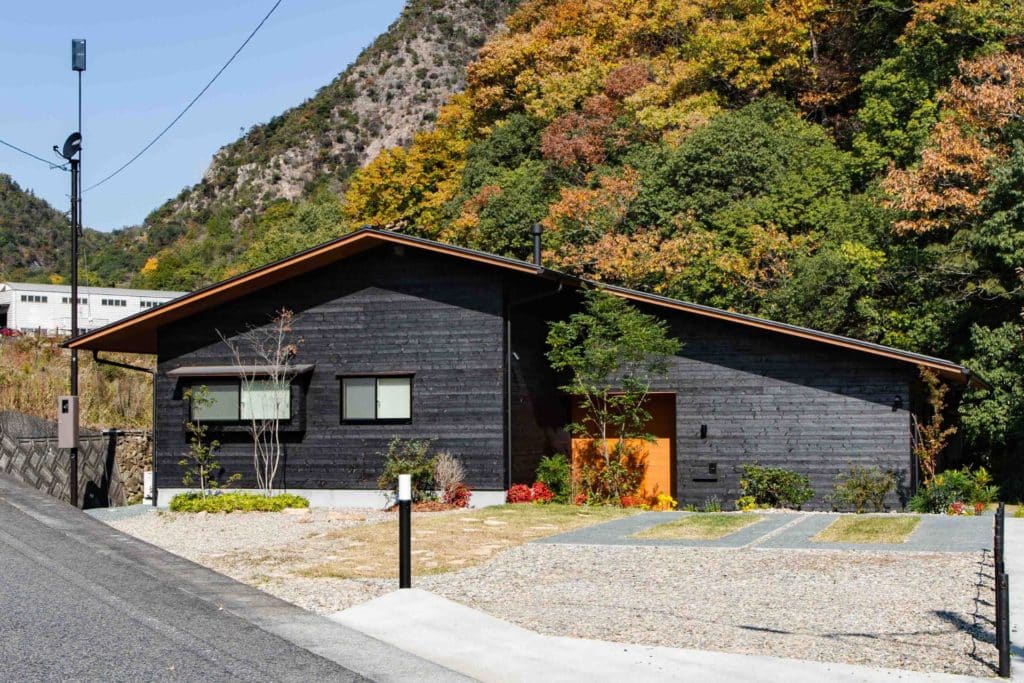 House with black wood on a street with trees and mountains in background