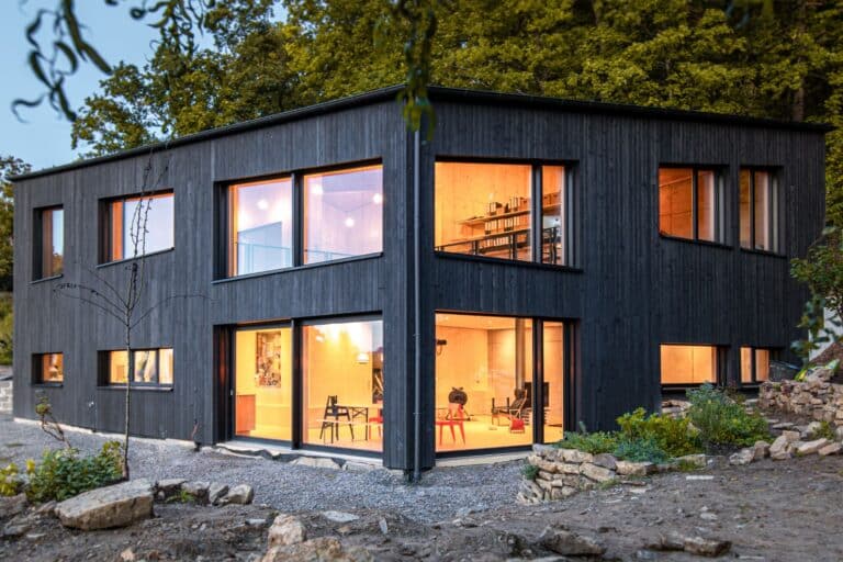 Maison moderne noire avec façade en bois dans la forêt.